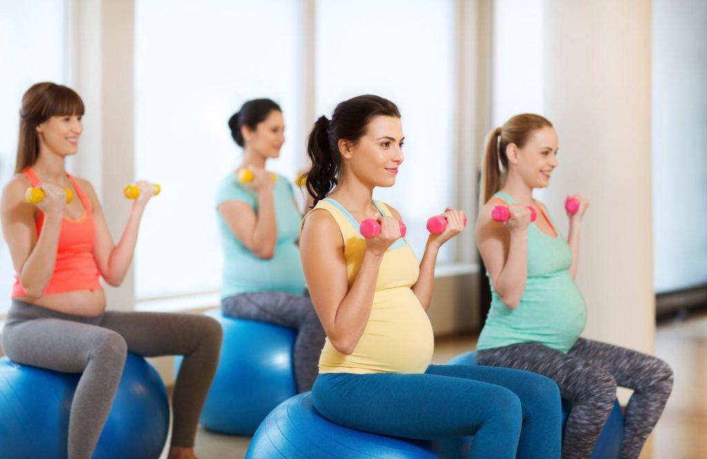pregnant women on exercise ball with light dumbbells