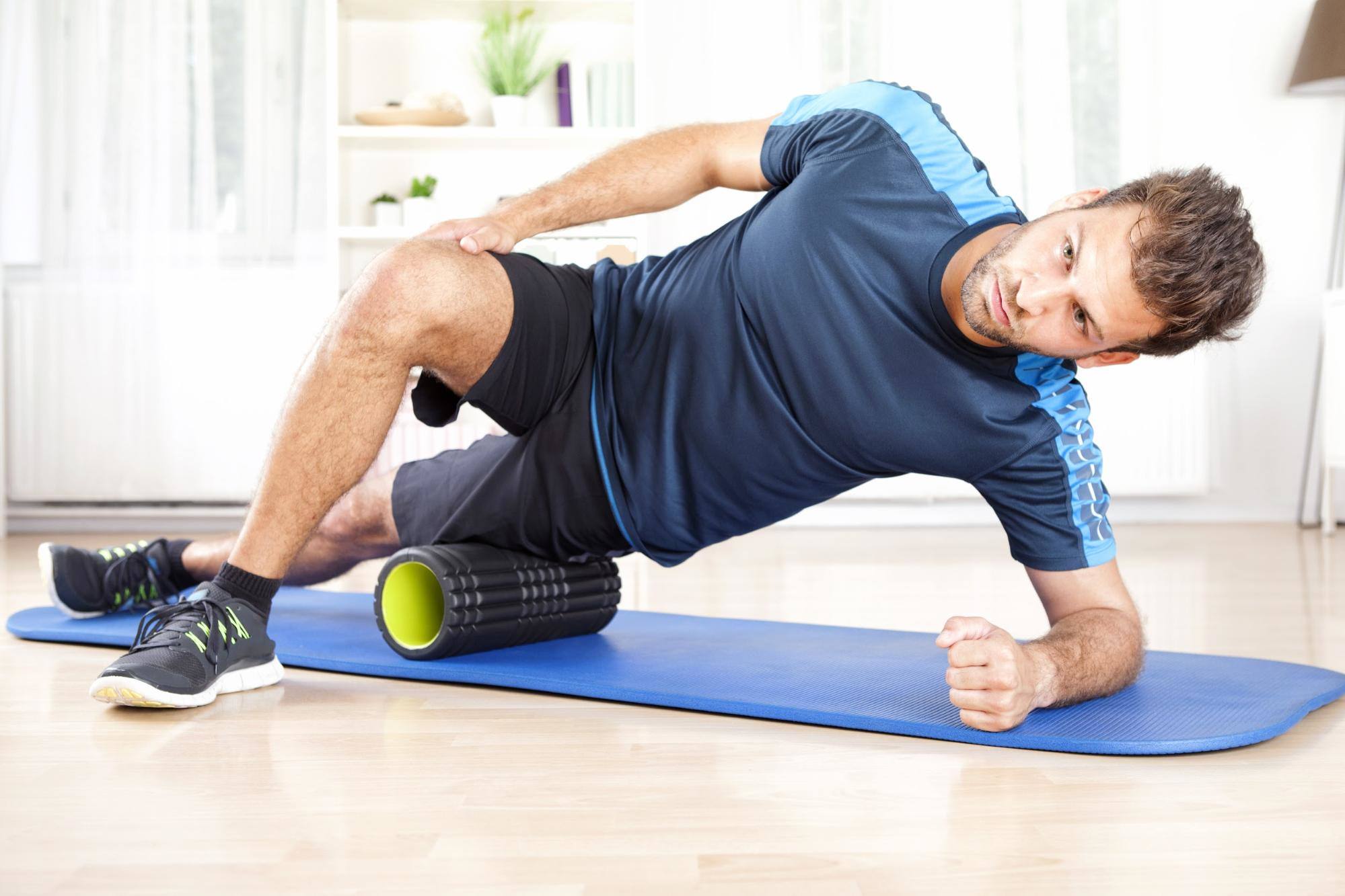 male in gym clothes using foam roller on his thigh