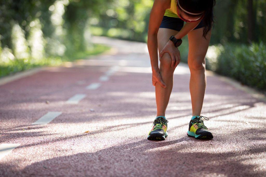 female runner on a running track rubbing her shin