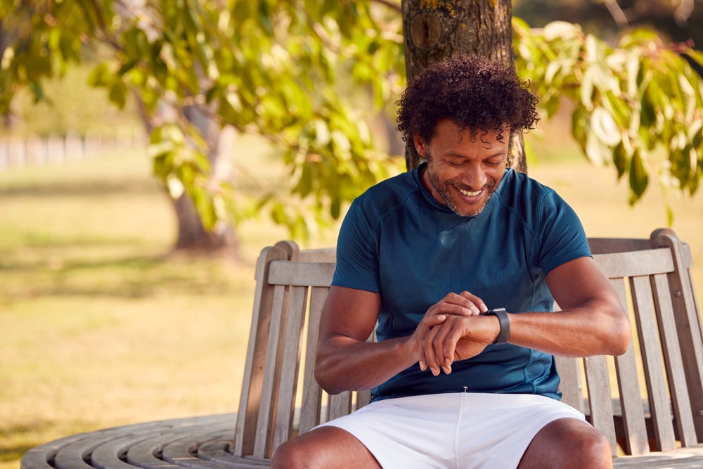 Man Looking at Fitness Watch While Seated Under a Tree